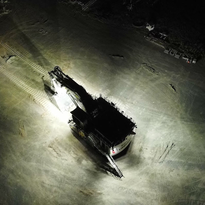 A vehicle on a dirt road at night with a spotlight illuminating the area.